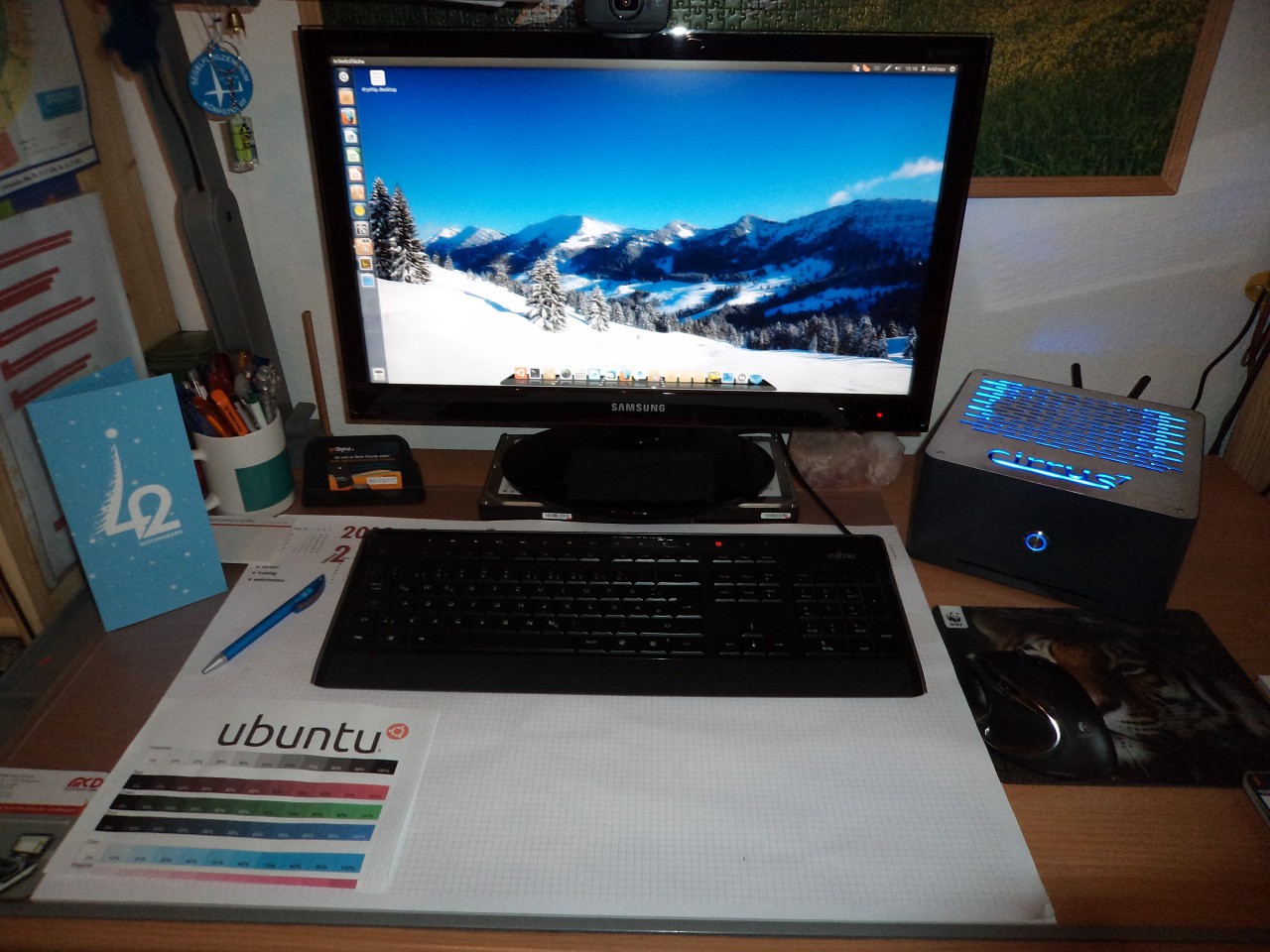 Ein Schreibtisch mit Monitor, Tastatur und dem cirrus7 One rechts daneben, dessen blau beleuchtete Deckplatte den Schriftzug cirrus7 zeigt