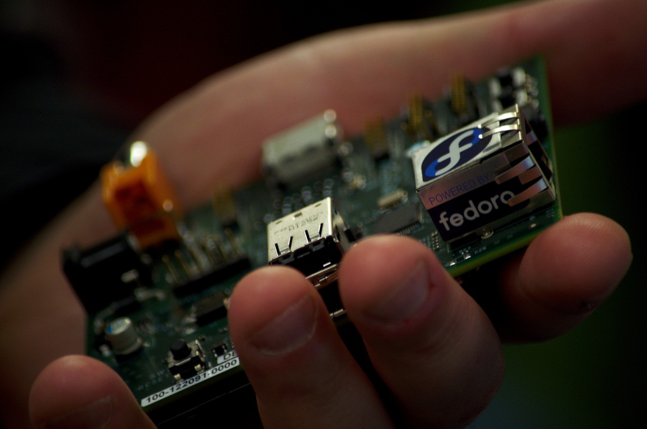 Eine Hand hält eine nackte Raspberry-Pi-Platine mit Netzwerkbuchse, USB-Anschlüssen und einem Fedora-Aufkleber