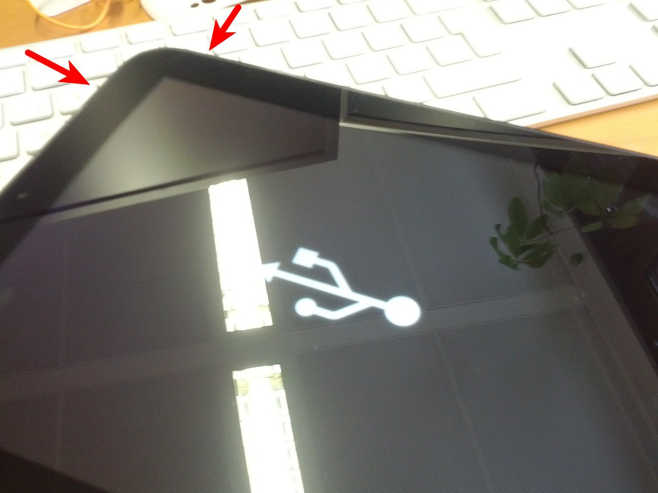 Das HP Touchpad zeigt ein großes USB-Symbol, zwei rote Pfeile markieren Ein-/Ausschalter und Lautstärkewippe