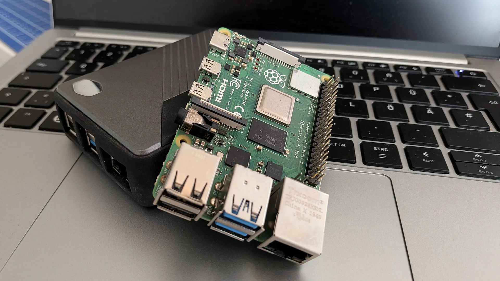 A Raspberry Pi 4 Model B leans against a black Pi case on the palm rest of a laptop.