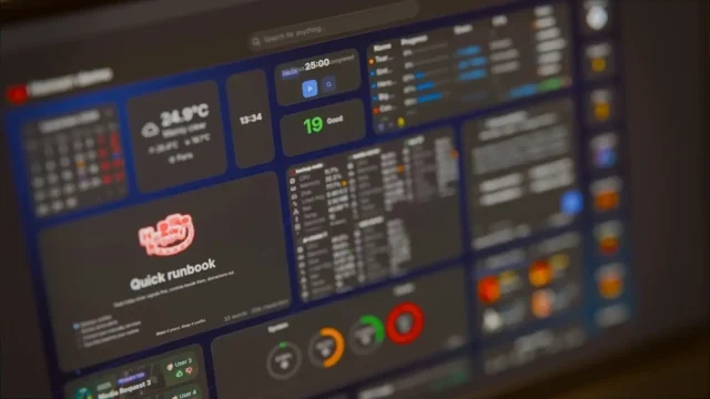 Schräg fotografierter Monitor mit einem dunklen Homarr-2.0-Dashboard, darauf Widgets für Wetter, Uhrzeit, Timer, Luftqualität, Downloads, Systemauslastung und ein Notizfeld.